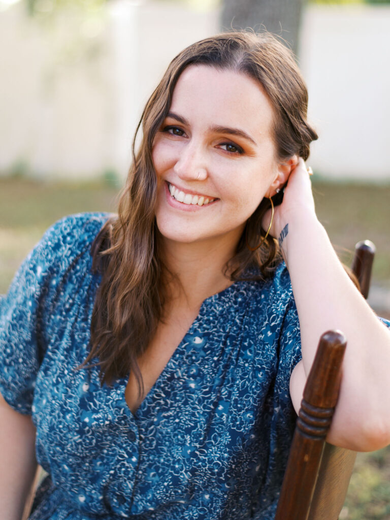 A brunette woman in a blue floral dress smiles at the camera