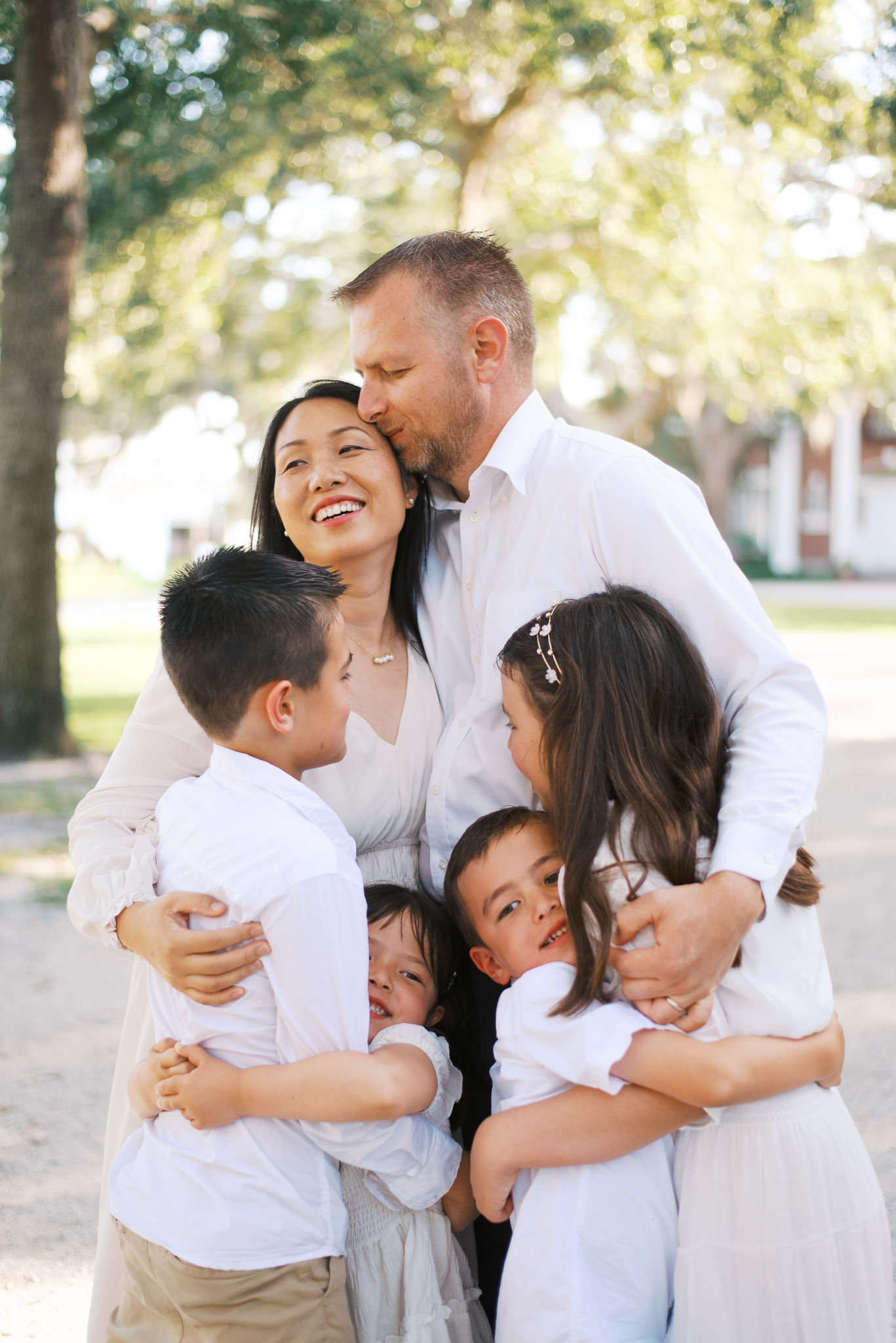 A husband and wife embrace their four young children and smile