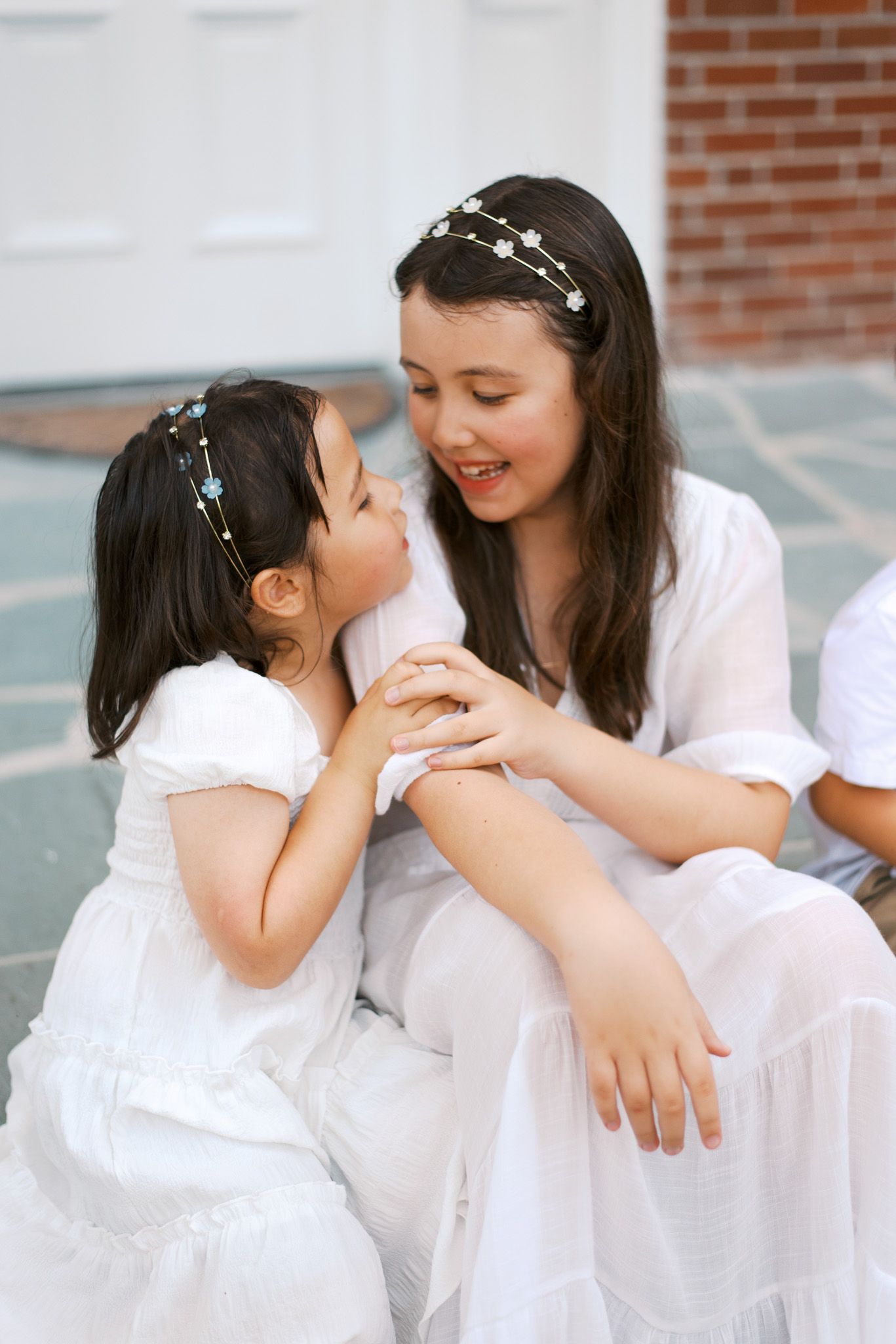 Two young sisters sit on a porch and lean into each other, laughing
