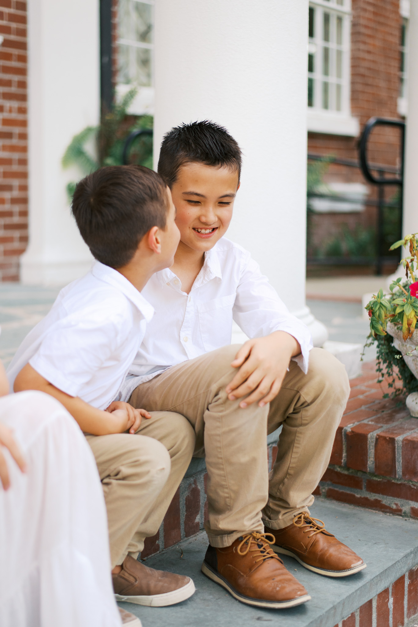 Two young brothers sit on a porch and smile while they talk to each other