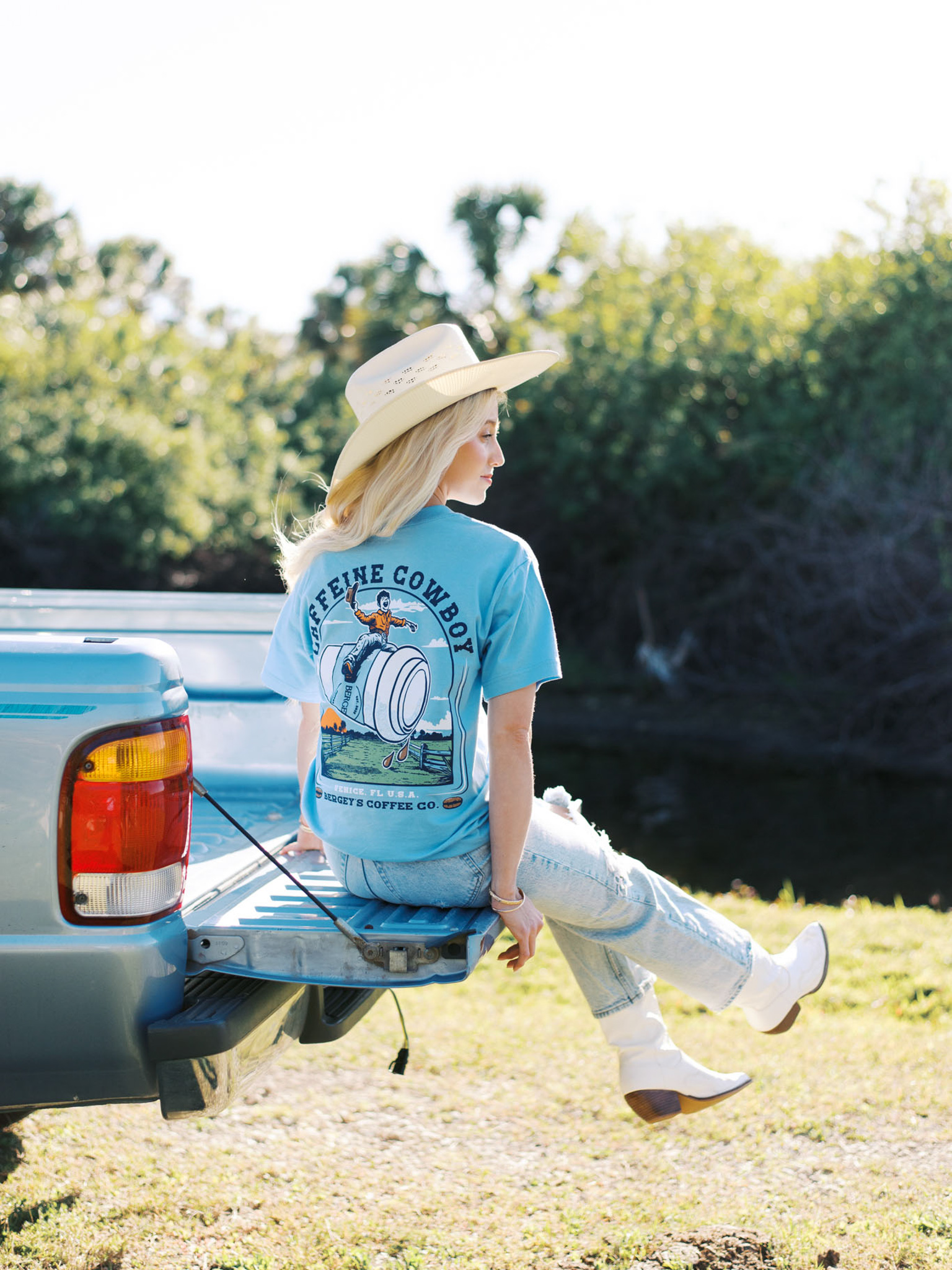 A blonde woman in a Bergey's Coffee shirt sits on the tailgate of a truck