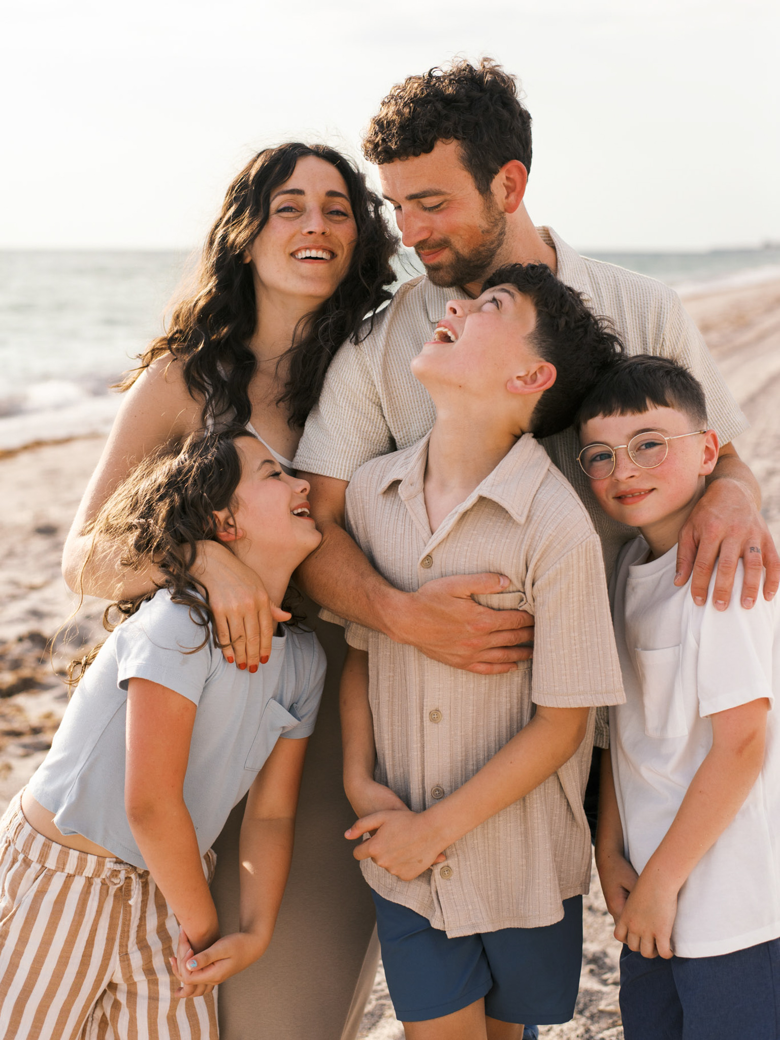 A young family of five leans into each other on the beach