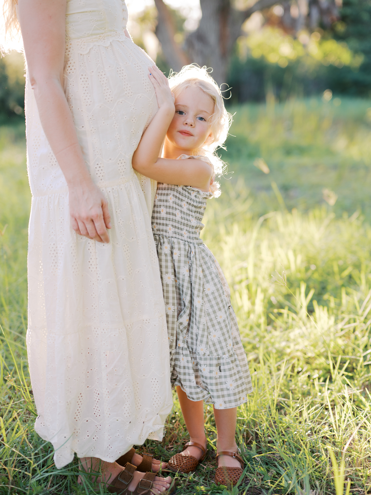 A young girl hugs her mom, holding her mom's baby bump